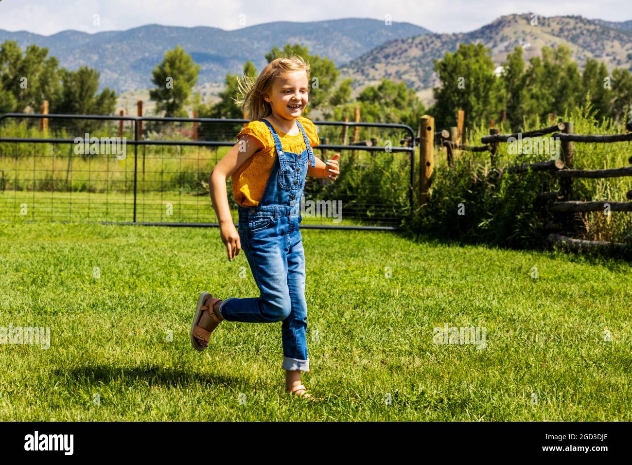 Junges Mädchen spielt und läuft im grasbewachsenen Hof Stockfoto