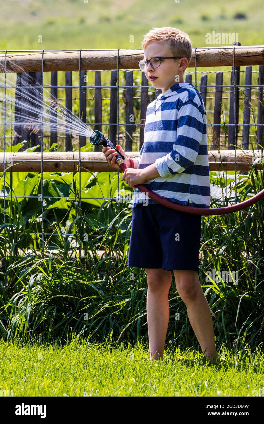 Kleiner Junge, der Wasser mit Gartenschlauch im grasbewachsenen Hof sprüht Stockfoto