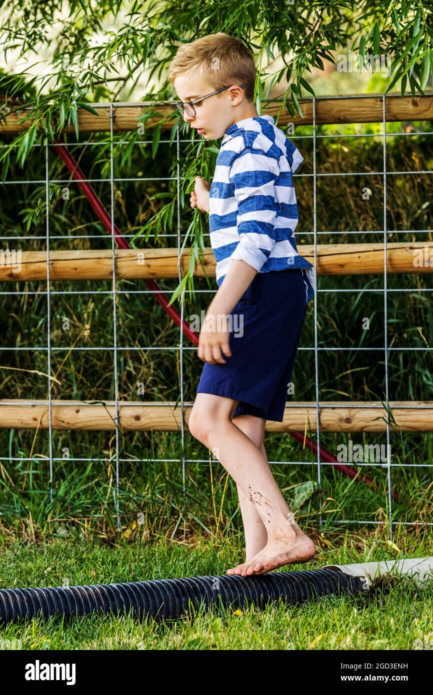 Kleiner Junge spielt und balanciert auf Drainagerohr im grasbewachsenen Hof Stockfoto