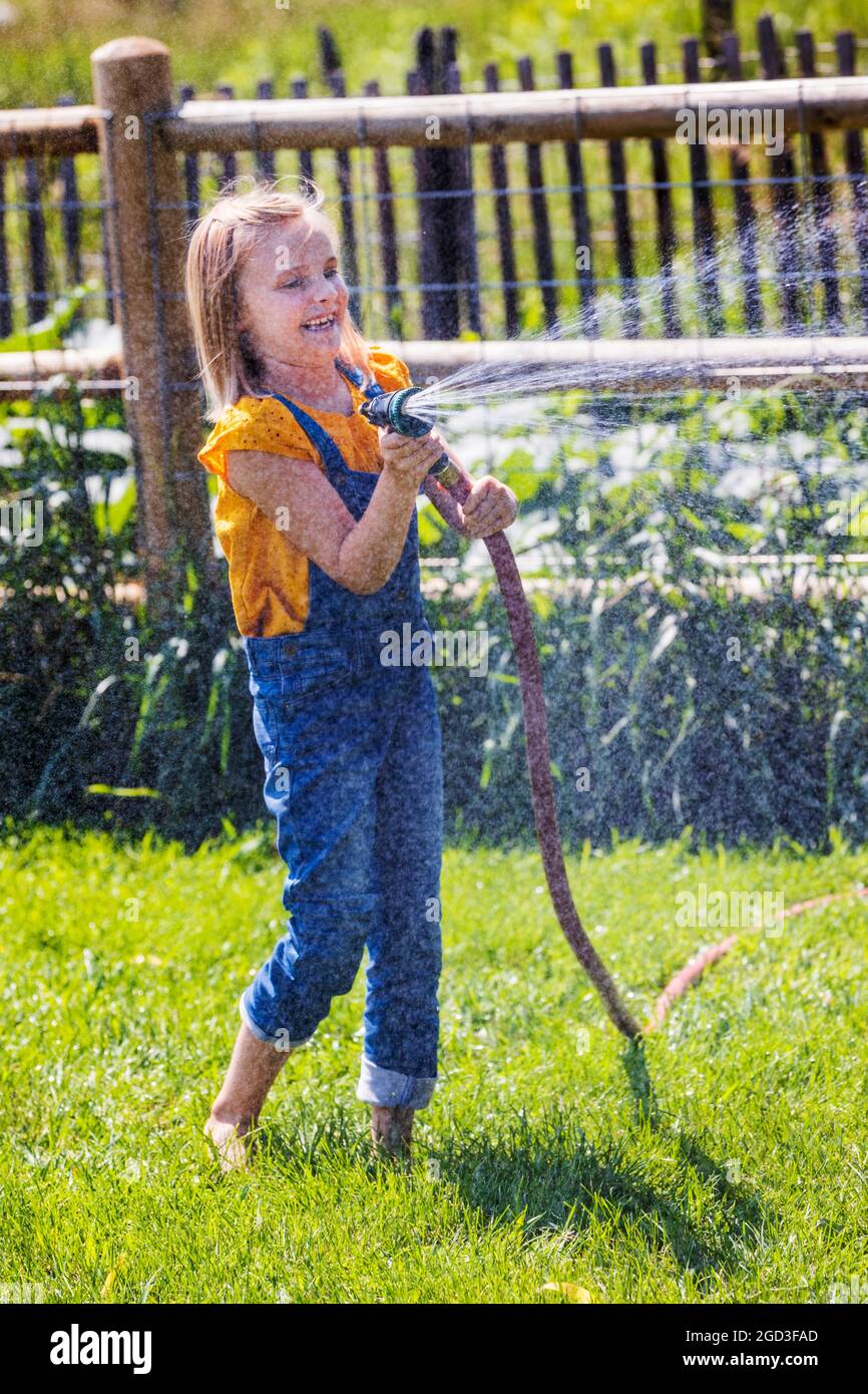 Junges Mädchen sprühen Wasser mit Gartenschlauch in grasbewachsenen Hof Stockfoto