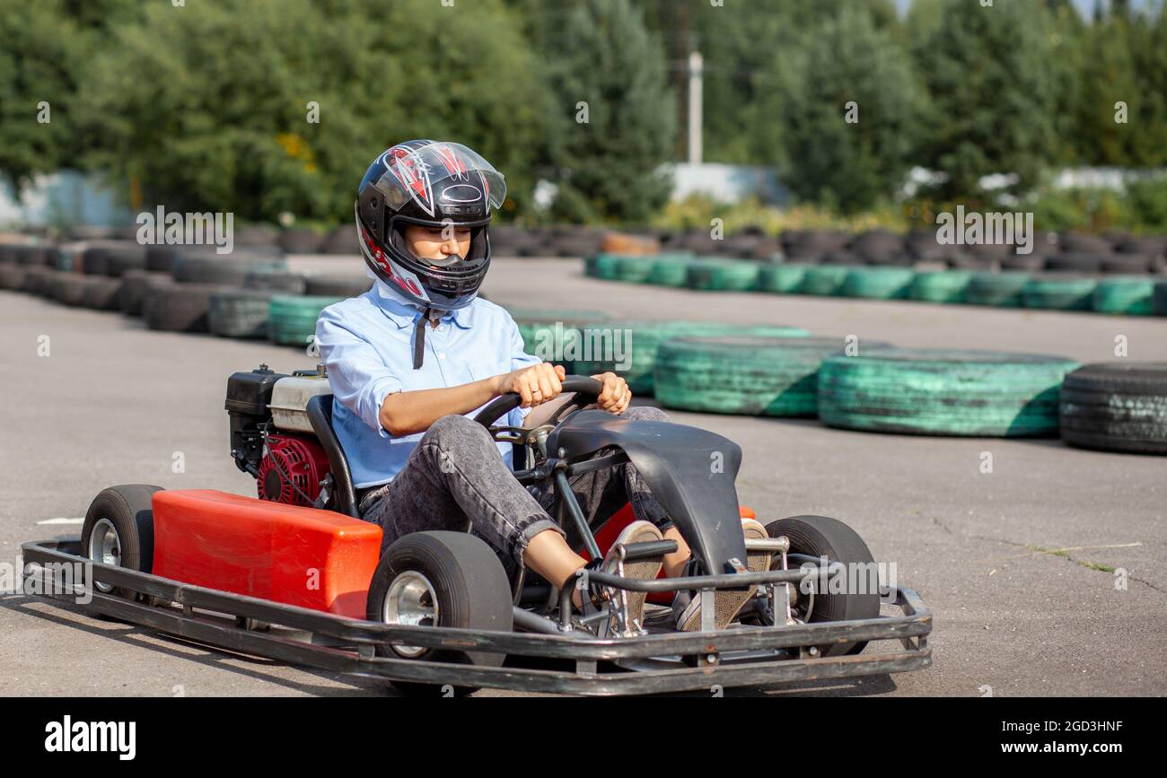 Ein Mädchen oder eine Frau in einem harten Hut reitet auf einer speziellen Strecke, die mit Gummirädern umzäunt ist, einen Go-Kart. Aktive Erholung und Sport auf Transport. Vorbereitung A Stockfoto