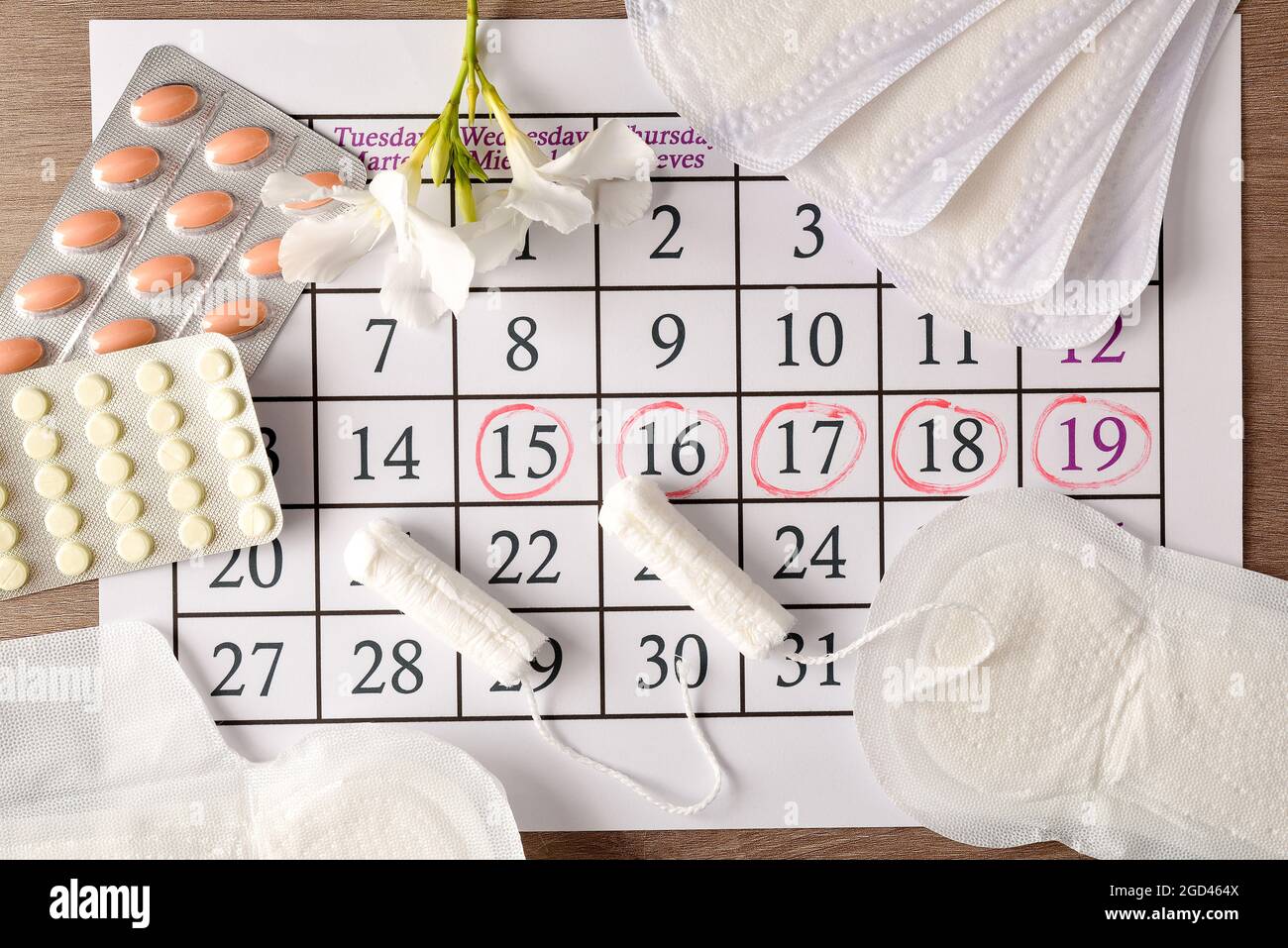 Menstruationskalender mit markierten kritischen Tagen und verschiedenen Menstruationshygieneprodukten und Pillen rund um auf Holztisch. Draufsicht. Stockfoto