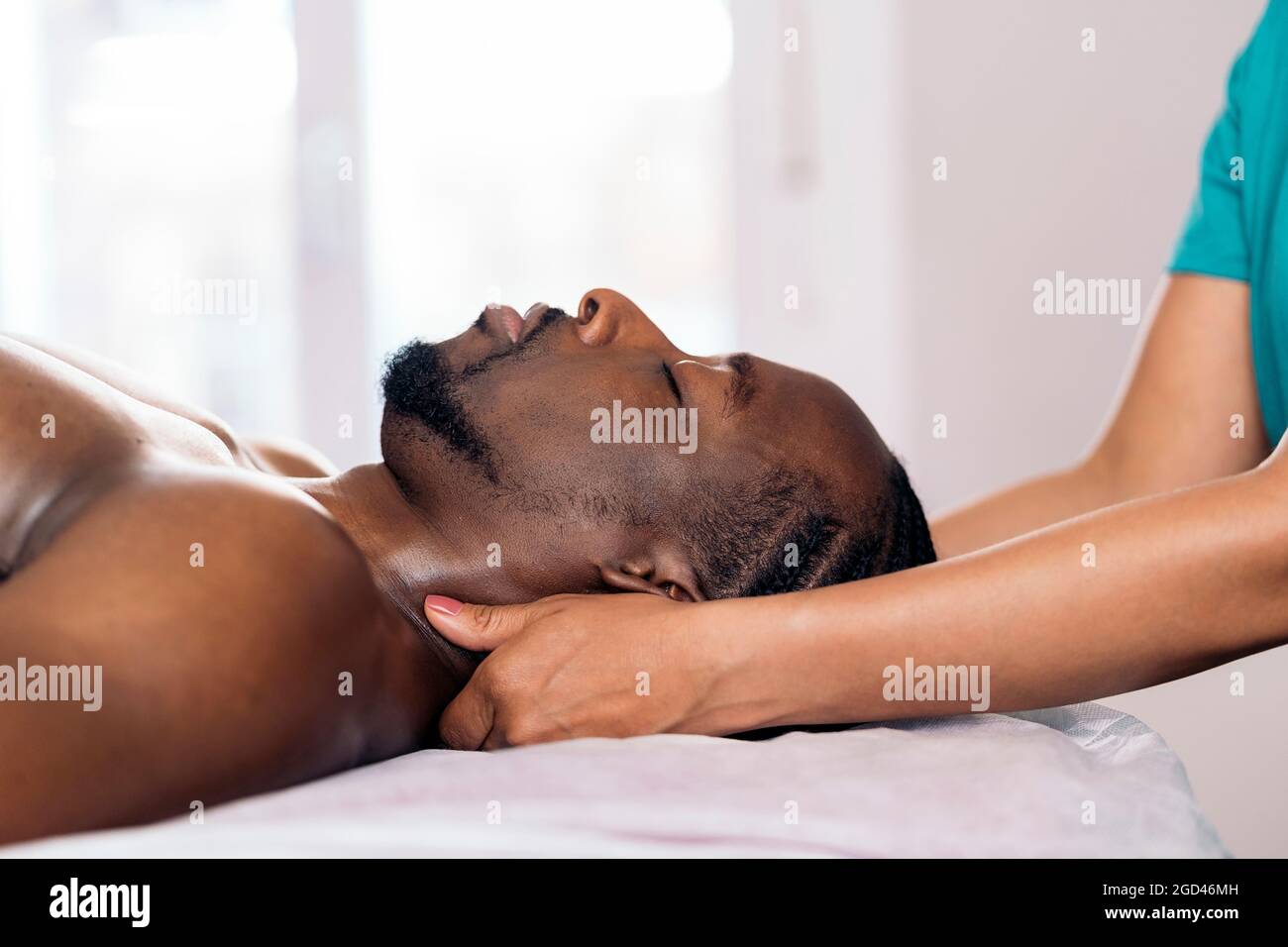 Entspannter schwarzer Mann, der sich hinlegt und eine Nackenmassage erhält. Die Masseuse verwendet eine Ölmassage. Stockfoto