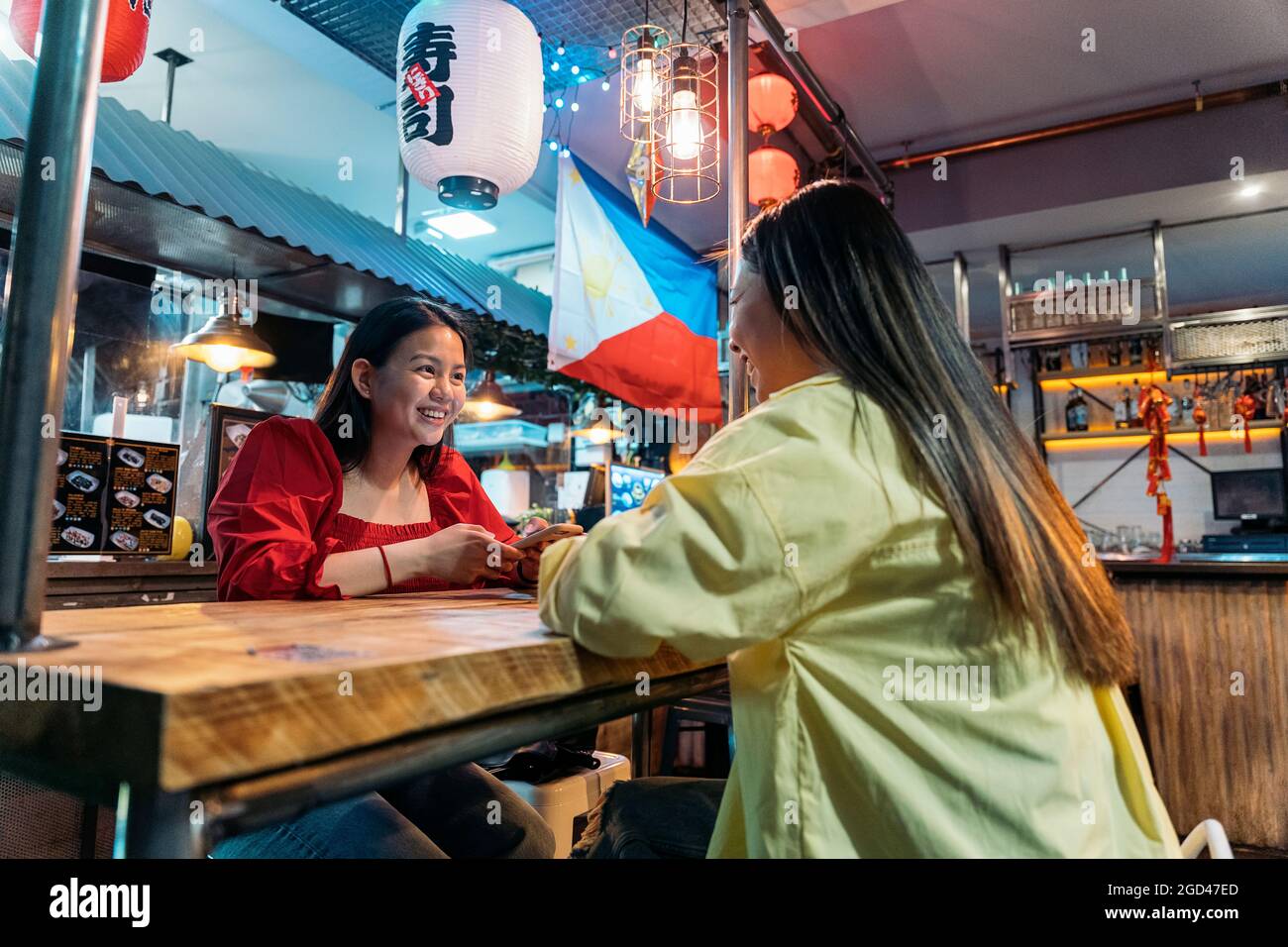 Glückliche asiatische Freundinnen, die im chinesischen Restaurant mit ihrem Telefon sitzen und sprechen. Stockfoto