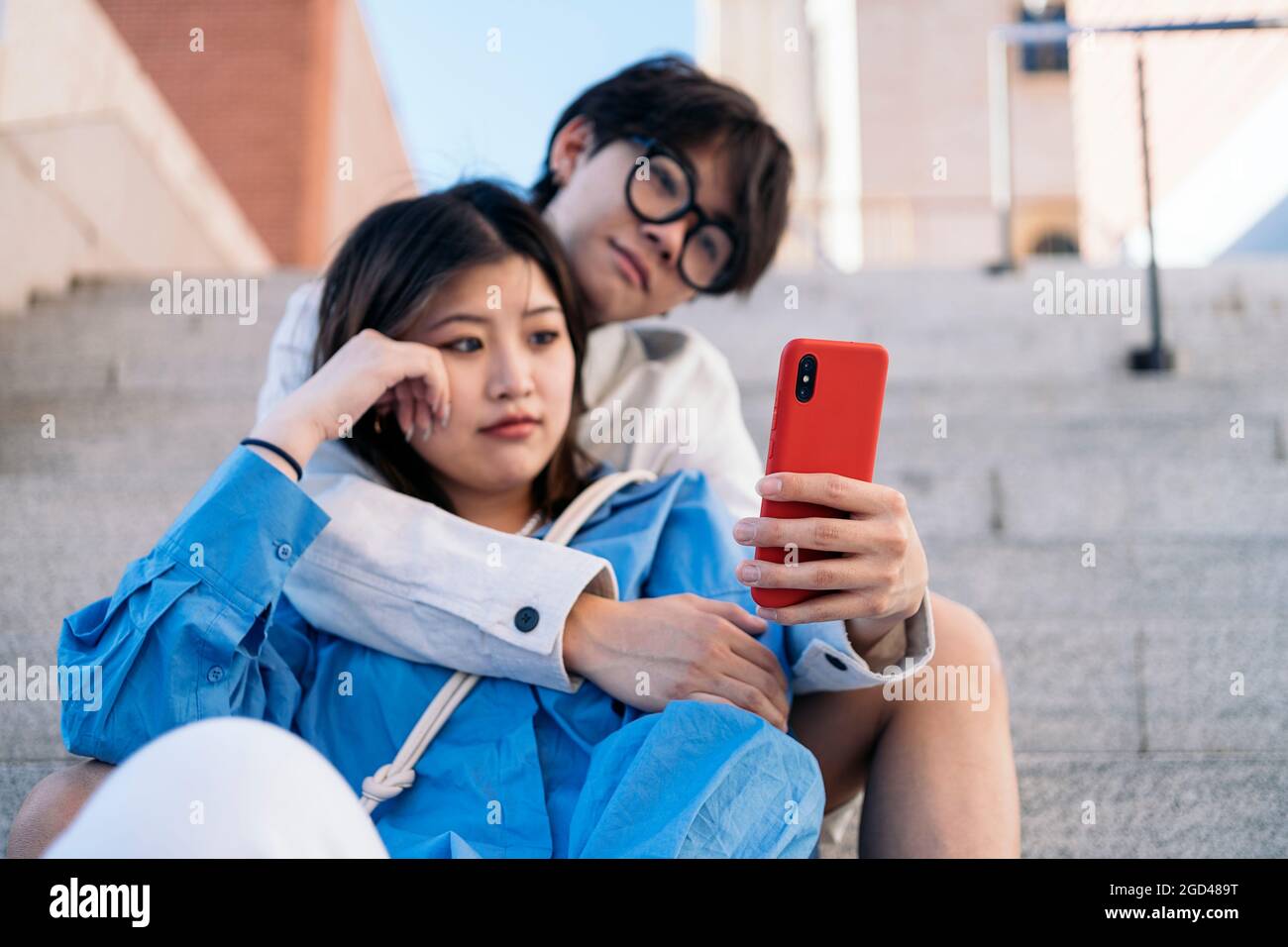Glückliches asiatisches Paar, das zusammen auf der Straße sitzt und auf ihr Smartphone schaut. Stockfoto