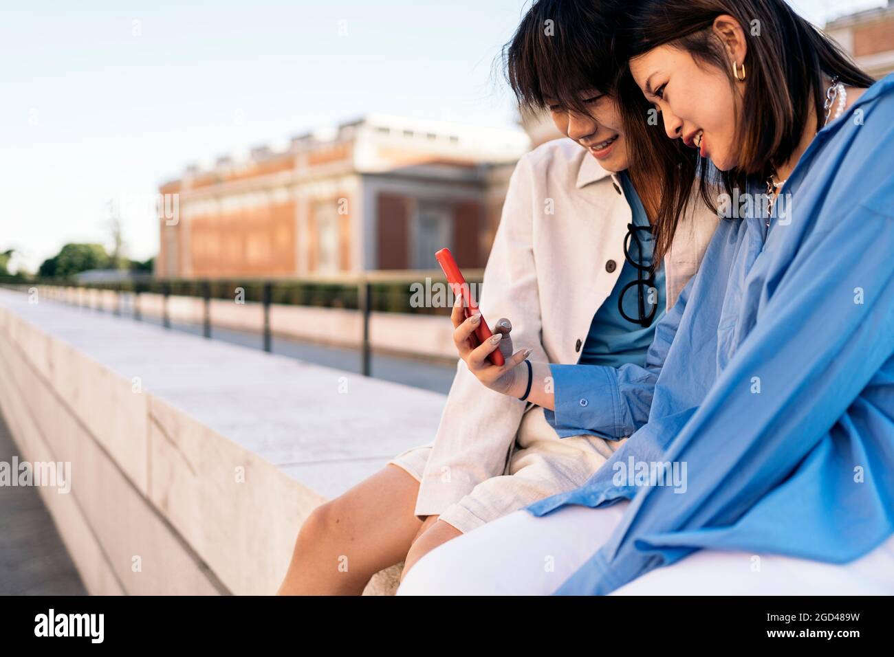 Glückliches asiatisches Paar, das zusammen auf der Straße sitzt und auf ihr Smartphone schaut. Stockfoto