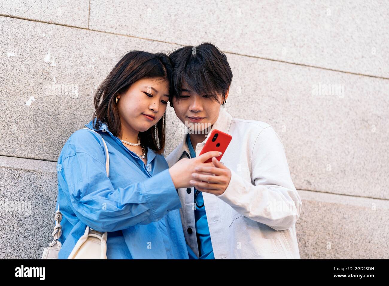 Cooles asiatisches Paar, das in der Stadt steht und auf ihr Telefon schaut. Stockfoto