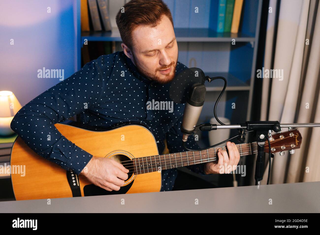 Mittellange Aufnahme eines gespielten Gitarristen-Sängers, der auf einer akustischen Gitarre spielt und in ein Mikrofon singt, um im Heimstudio einen Song aufzunehmen. Stockfoto