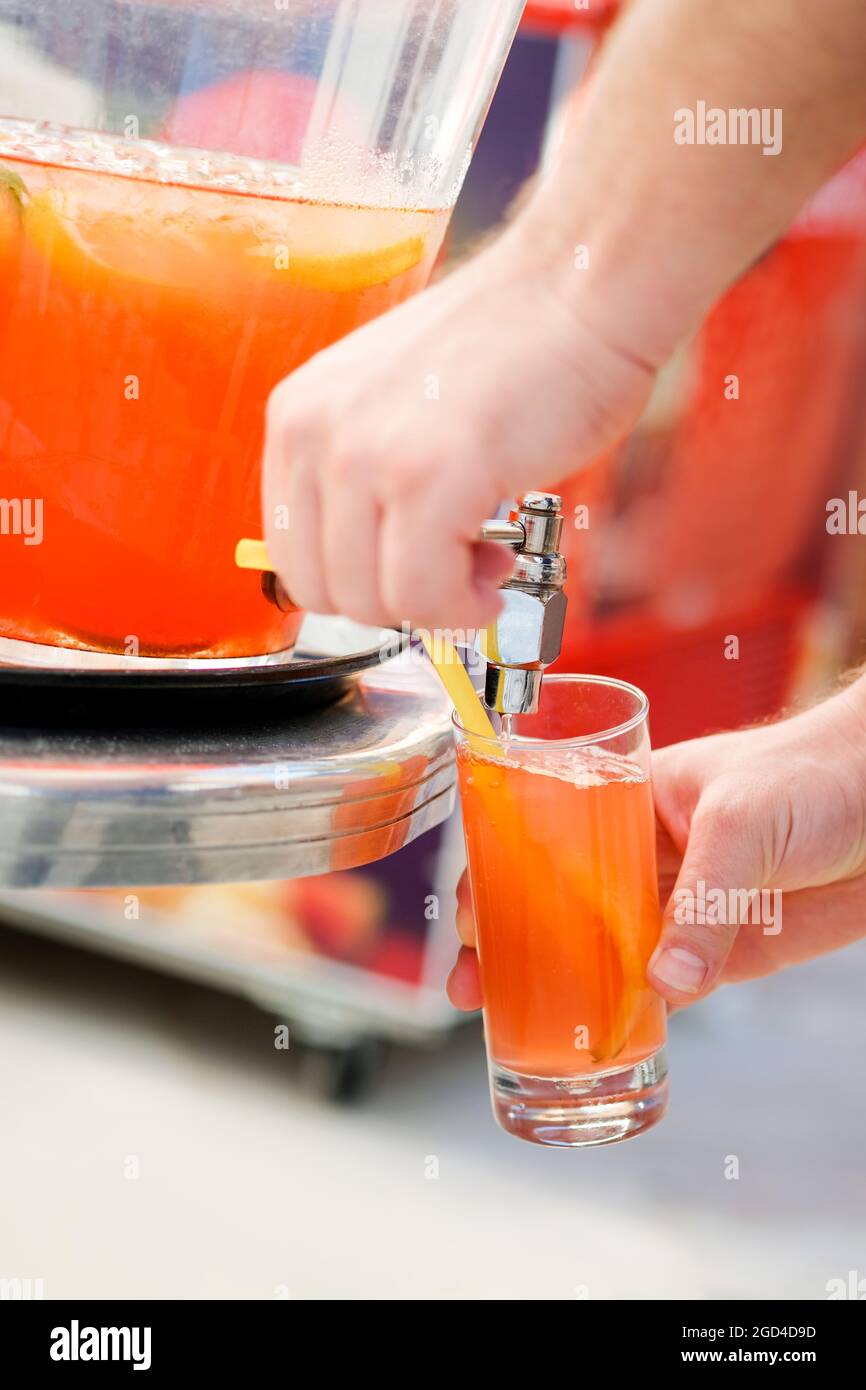 Mann gießt frischen Sorbet-Fruchtsaft oder Alkoholpunsch aus der Trinkgefäßmaschine auf der Party. Stockfoto