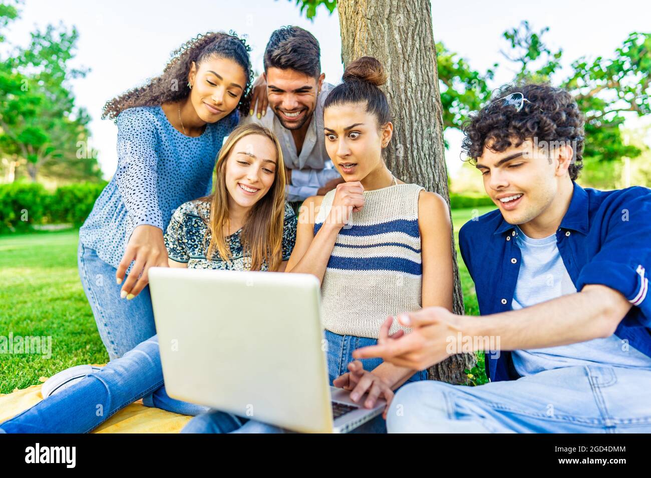 Junge Hipster-Freunde sitzen auf dem Rasen im Stadtpark machen Überraschung Gesichter suchen Laptop-Bildschirm. Modernes Fun-Konzept mit Millennials auf neuem Trend Stockfoto