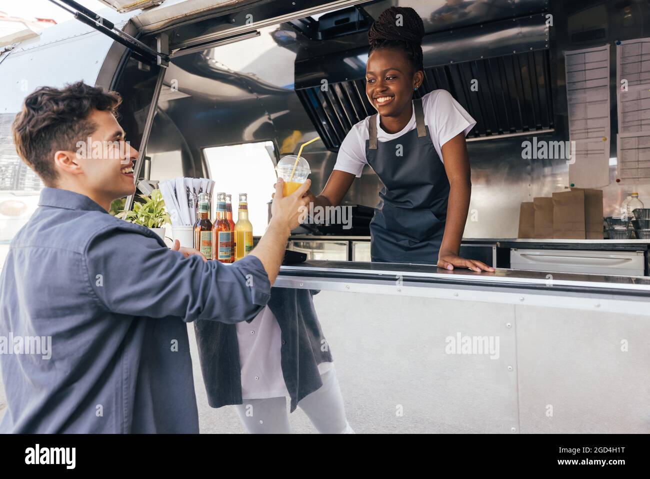 Besitzer des Food-Trucks, der den Kunden ansieht. Lächelnder Kunde, der von der Verkäuferin ein Getränk erhält. Stockfoto