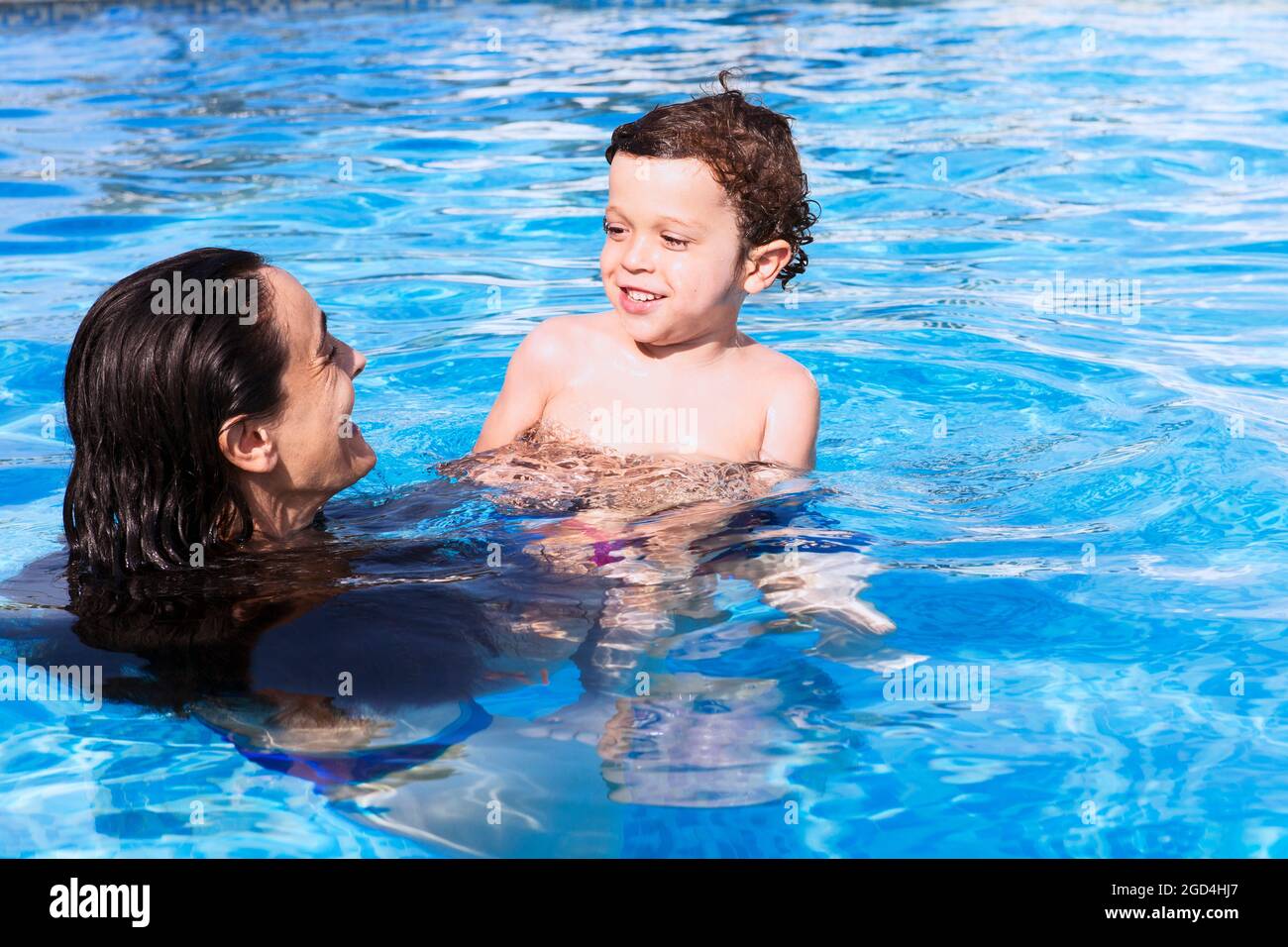 Mutter und Sohn badeten im Pool, beide lächelten und schauten sich beim Genießen fröhlich an Stockfoto