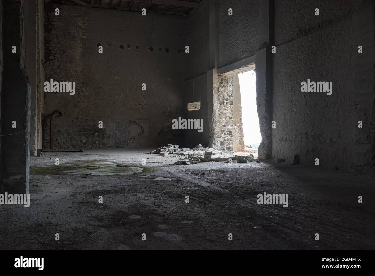 Verlassene industrielle Innenausstattung. Dunkles, leeres Lagerhaus mit rissigen Betonwänden, zerbrochenen Ziegelsteinen und Licht, das durch die offene Tür fällt Stockfoto
