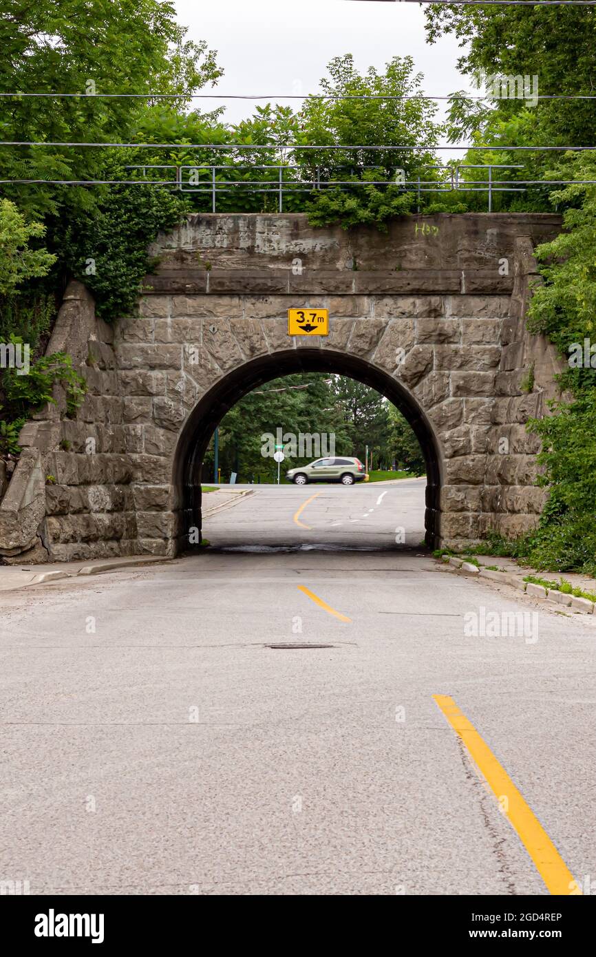 Vertikaler selektiver Fokus auf Steinautobahn unter einer Eisenbahnbrücke. Unscharfes Auto im Hintergrund, Straßenlinie im Vordergrund. Stockfoto