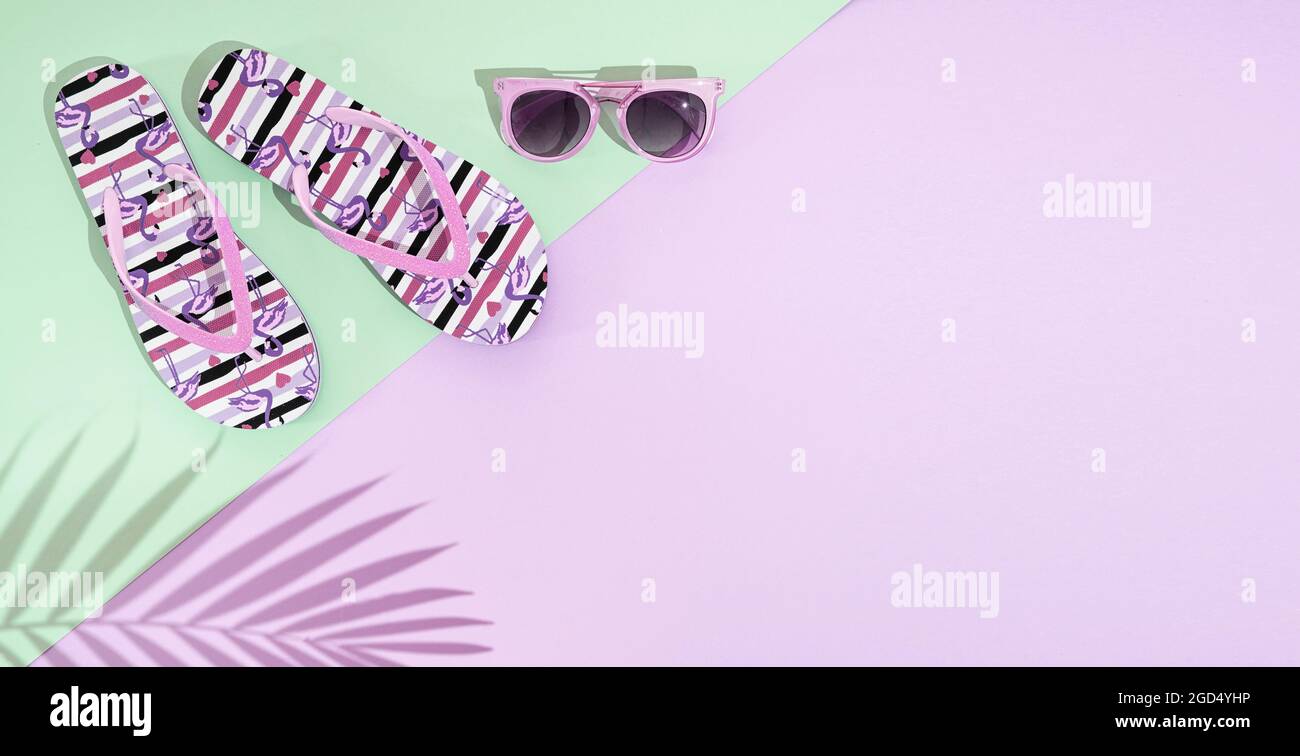 Ein Paar Sommersandalen, Flip Flop und rosa Sonnenbrillen auf pastellrosa und grünem Hintergrund mit Palmblatt-Schatten, Draufsicht, Kopierraum Stockfoto
