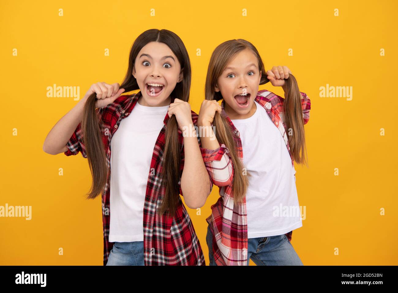 Verblüffte Kinder im lässigen karierten Hemd halten lange, gerade Haare auf gelbem Hintergrund, Frisur Stockfoto