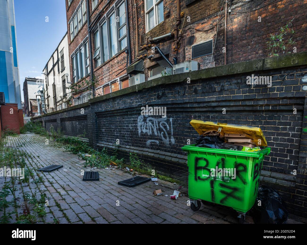 Eine hintere Gasse mit alten und neuen Gebäuden mit hellem Dayglo-Mülltonne. Stockfoto