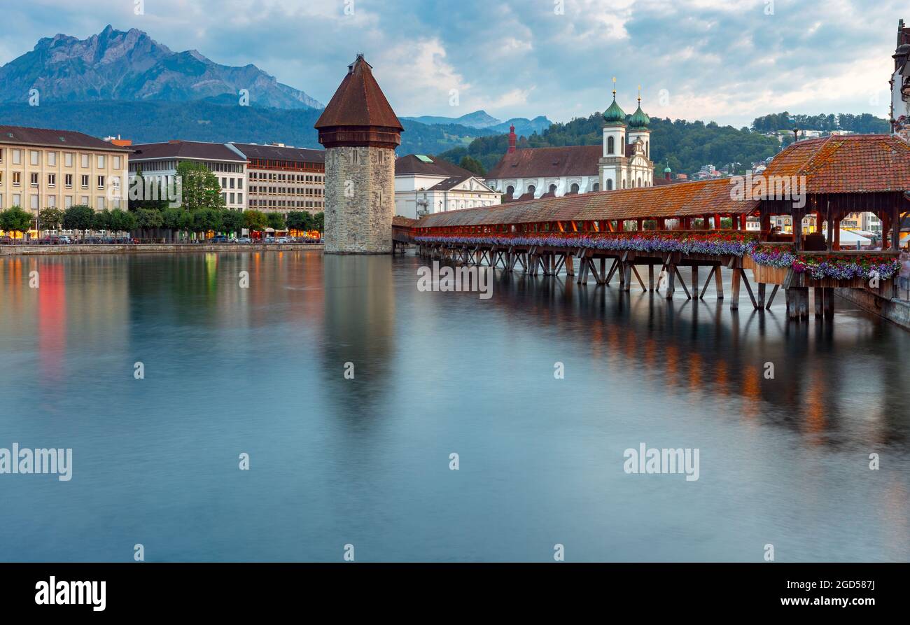 Panoramablick auf die Kirche, die hölzerne Kapellbrucke-Brücke im Licht der Laternen bei Sonnenaufgang. Luzern. Schweiz. Stockfoto