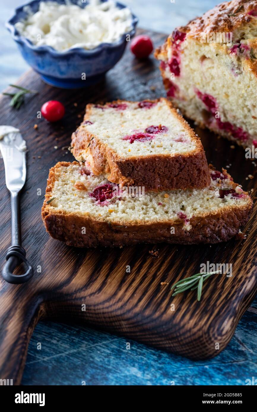 Nahaufnahme eines in Scheiben geschnittenen Cranberry Rosmarin-Schnellbrotes mit Frischkäse, der sich hinten einstreckte. Stockfoto