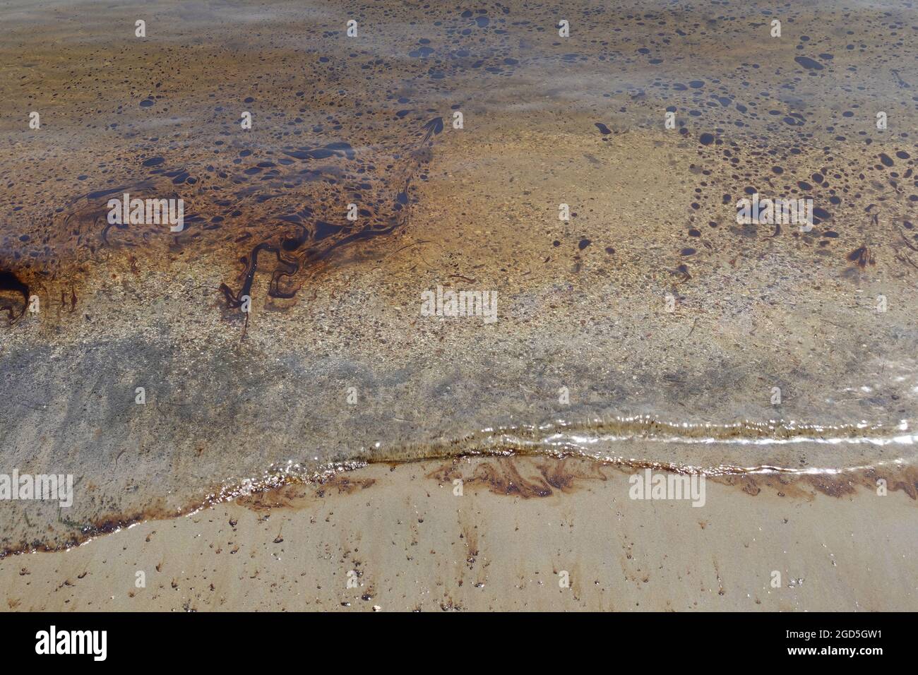 Schwarzes Teeröl schwimmt auf dem Meerwasser des verschmutzten Sandstrandes. Stockfoto