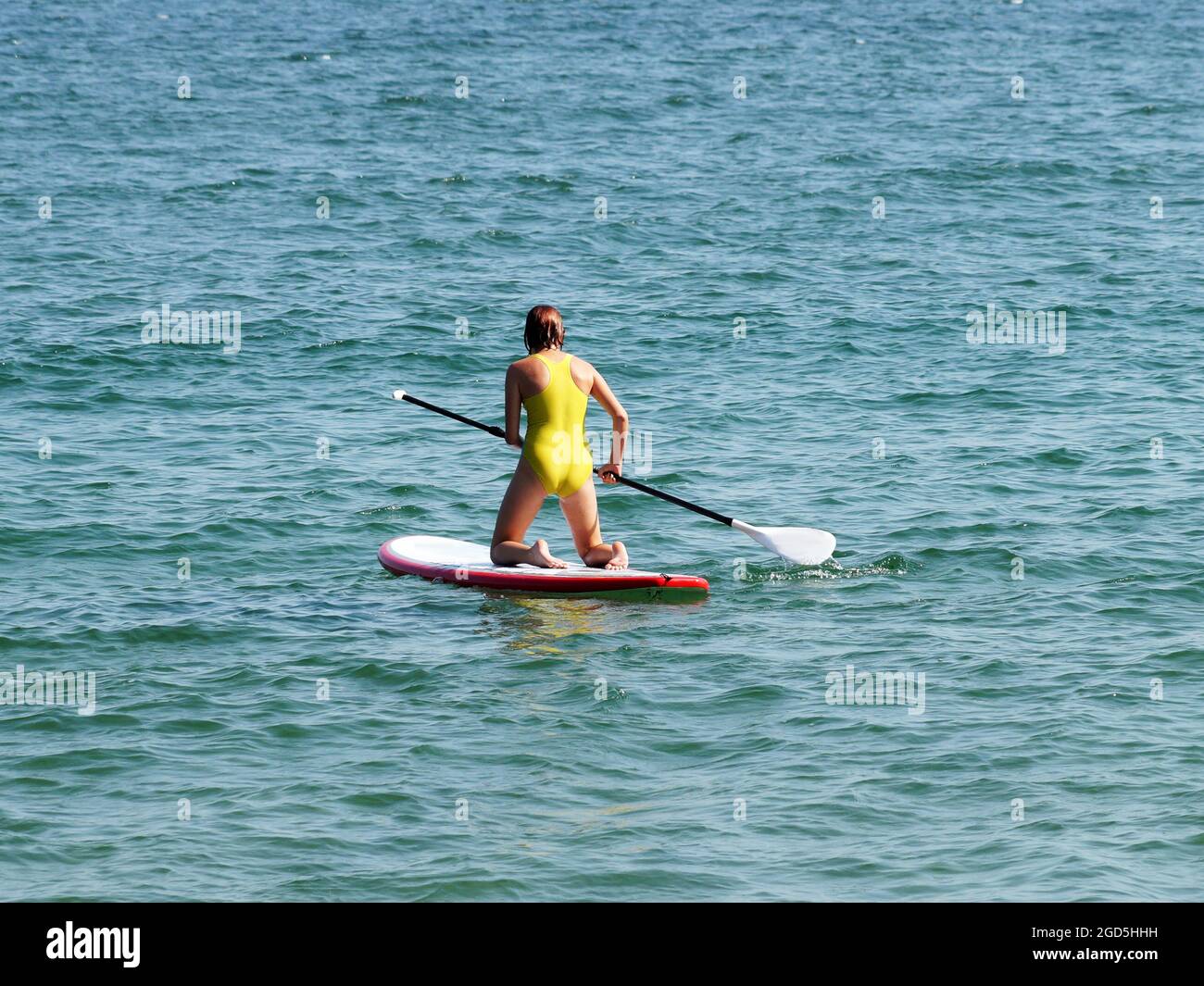 Teenager-Mädchen, das auf ihren Knien auf einem Brett im Meer reitet. Stockfoto