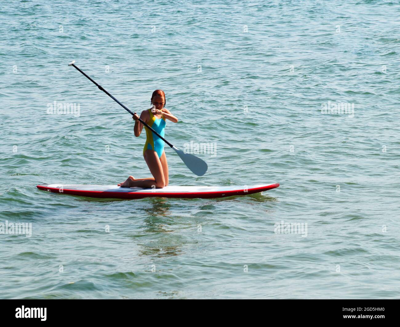 Teenager-Mädchen, das auf ihren Knien auf einem Brett im Meer reitet. Stockfoto