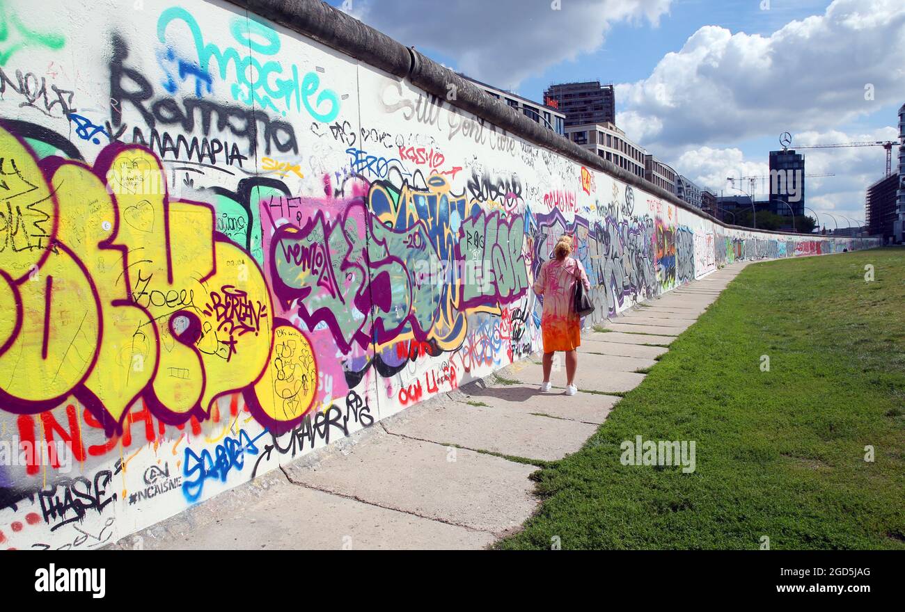 Berlin, Deutschland. August 2021. Eine Frau betrachtet die bemalten Betonteile der Berliner Mauer in der East Side Gallery im Stadtteil Friedrichshain-Kreuzberg. Am 13. August 2021 jährt sich der Bau der Berliner Mauer zum 60. Mal. Quelle: Wolfgang Kumm/dpa/Alamy Live News Stockfoto