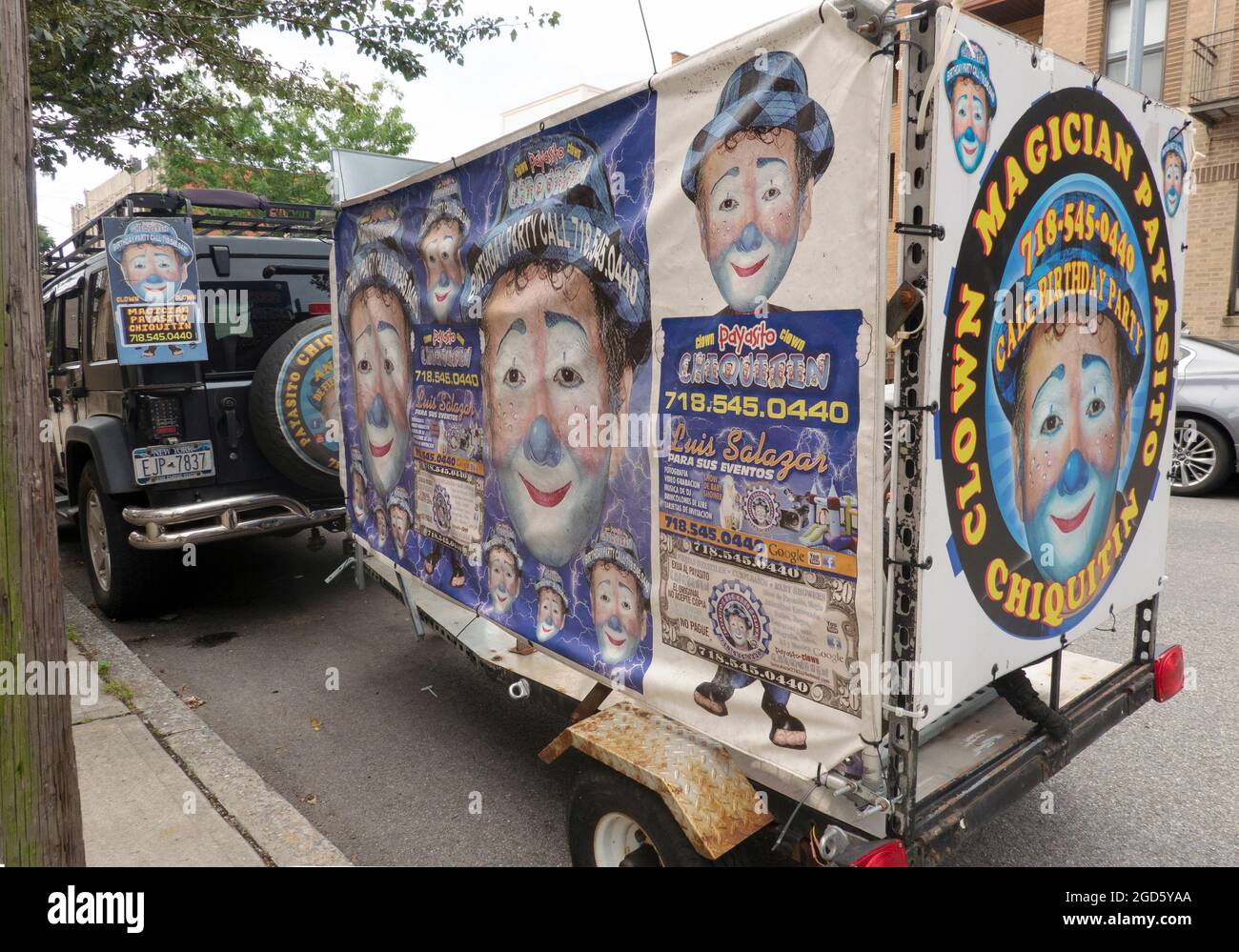 Ein SUV und Trailer mit farbenfrohen Anzeigen für Payasito Chiquitin, einen spanischsprachigen Clown, Zauberer und Entertainer. In Astoria, Queens, New York. Stockfoto
