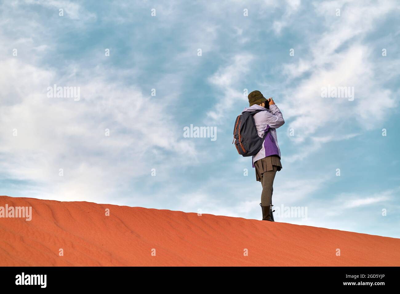 asiatische Fotografin, die auf einer Sanddüne steht und ein Bild fotografiert Stockfoto
