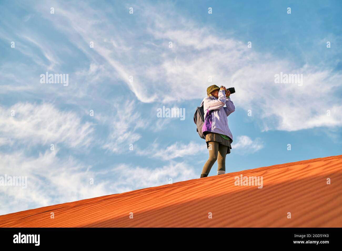asiatische Fotografin, die auf einer Sanddüne steht und ein Bild fotografiert Stockfoto
