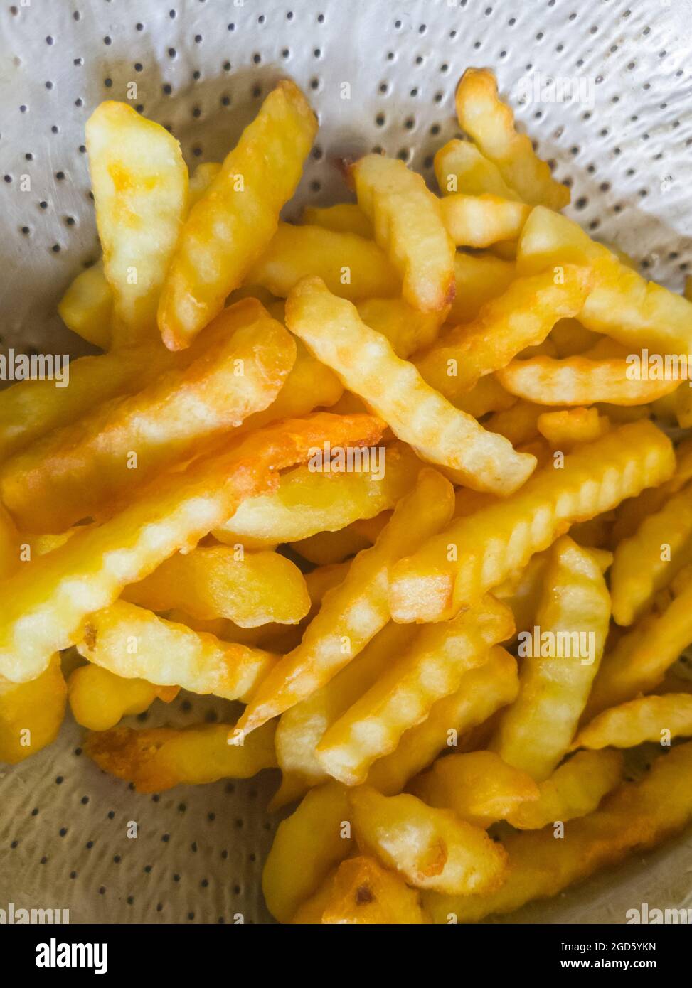 Die goldenen pommes frites im Metallsieb nach dem Kochen zum Salzen vorbereiten, bevor sie im lokalen Restaurant serviert werden, Vorderansicht für den Backgro Stockfoto