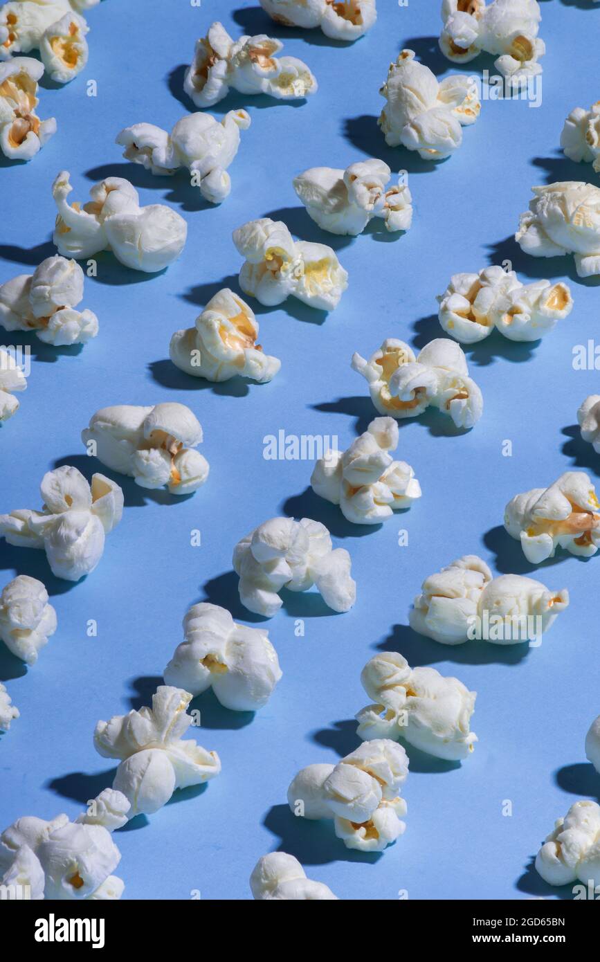 Durchgehend blauer Hintergrund mit weißem Popcorn, in diagonalen Reihen aufgereiht, minimalistischer Stil, keine Menschen Stockfoto