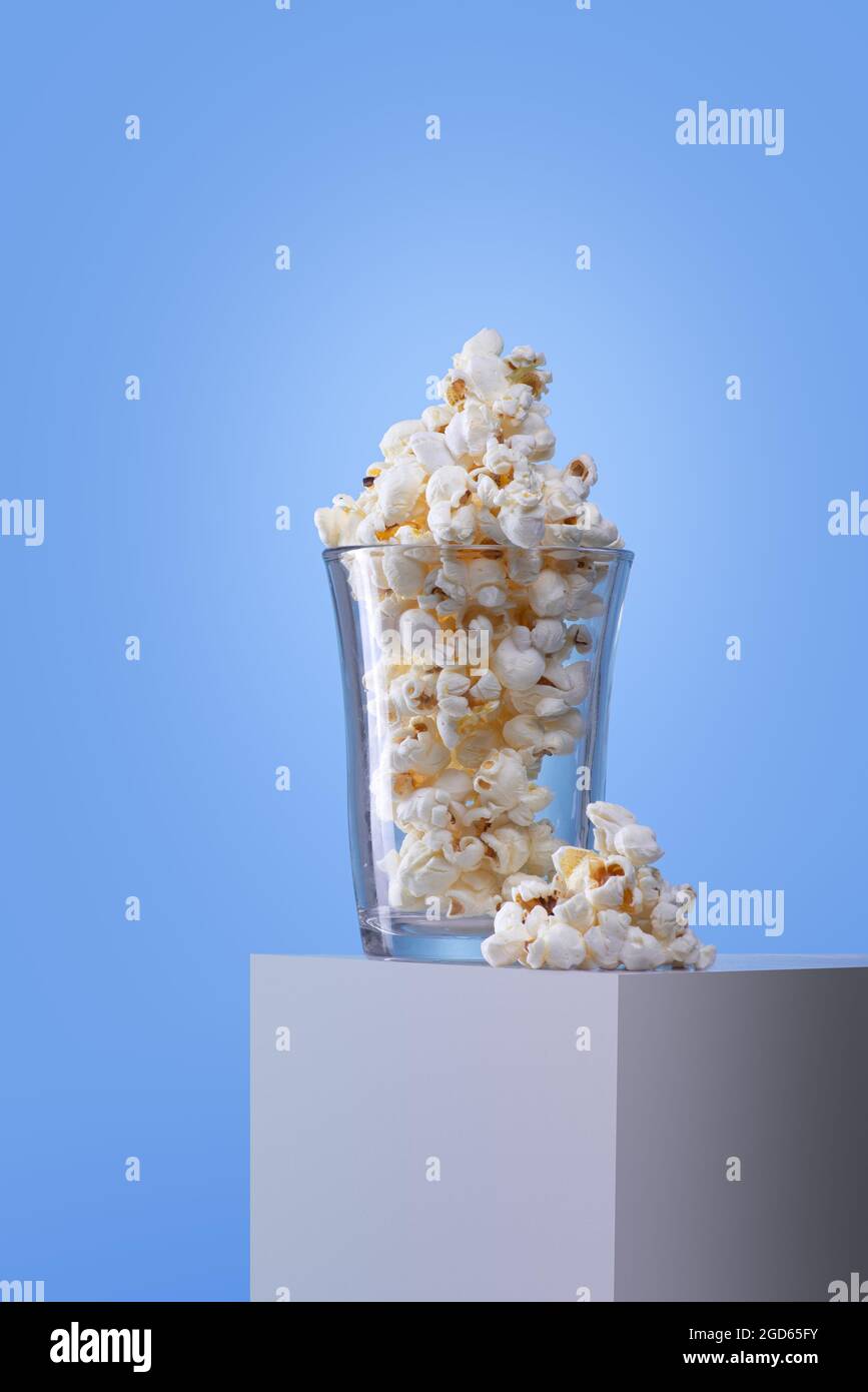 Kristallglas mit Popcorn auf einer weißen Schachtel und blauem Hintergrund; keine Menschen Stockfoto
