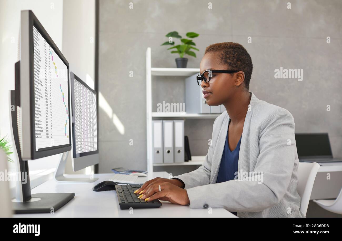Junge Geschäftsfrau oder Buchhalterin, die am Schreibtisch sitzt und an Computern arbeitet Stockfoto