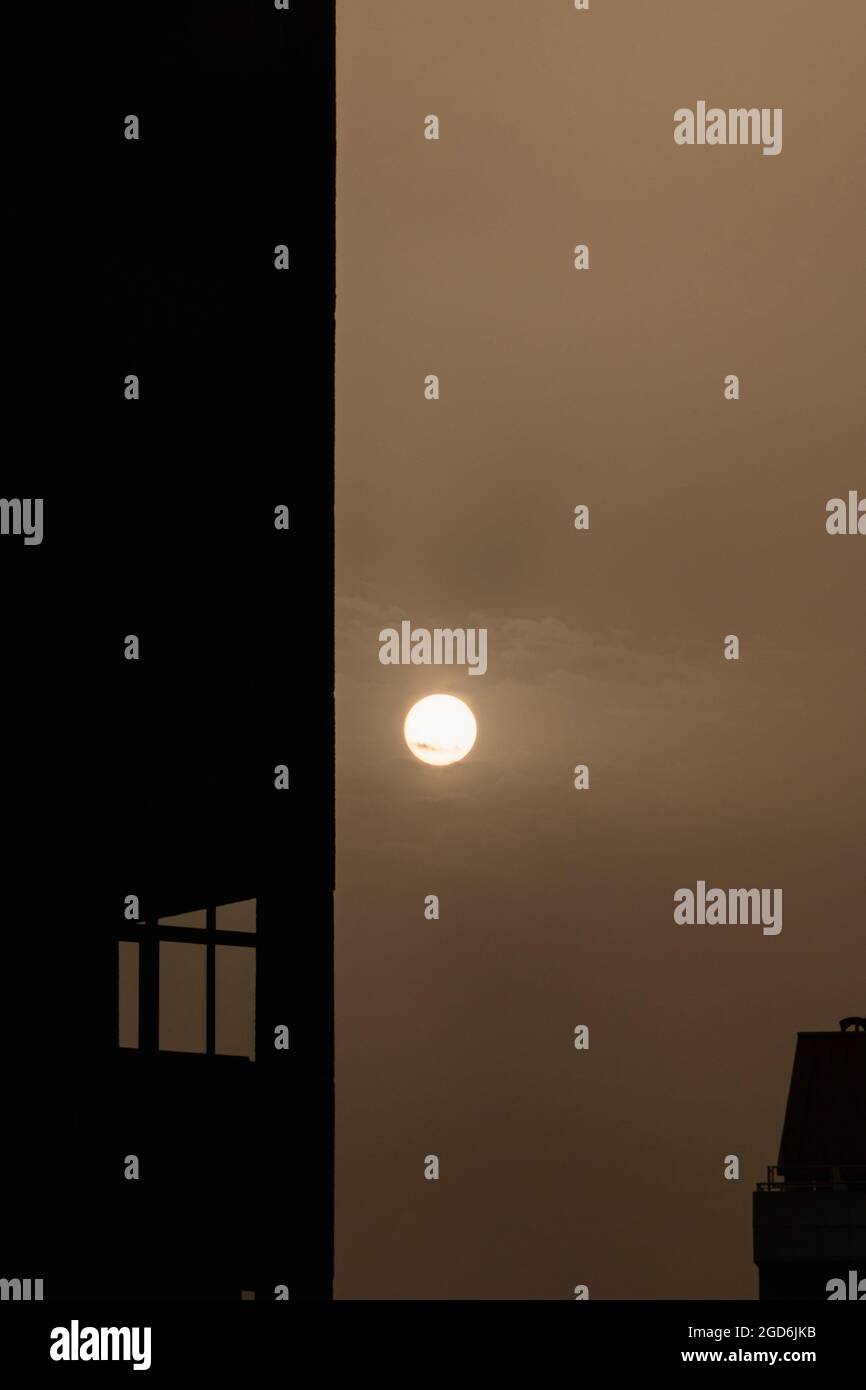 Sonnenaufgang mit einem bewölkten Himmel und einigen dünnen Wolken. In den Ecken sieht man die Silhouetten einiger Gebäude und Fenster. Die Atmosphäre ist dunkel und o Stockfoto