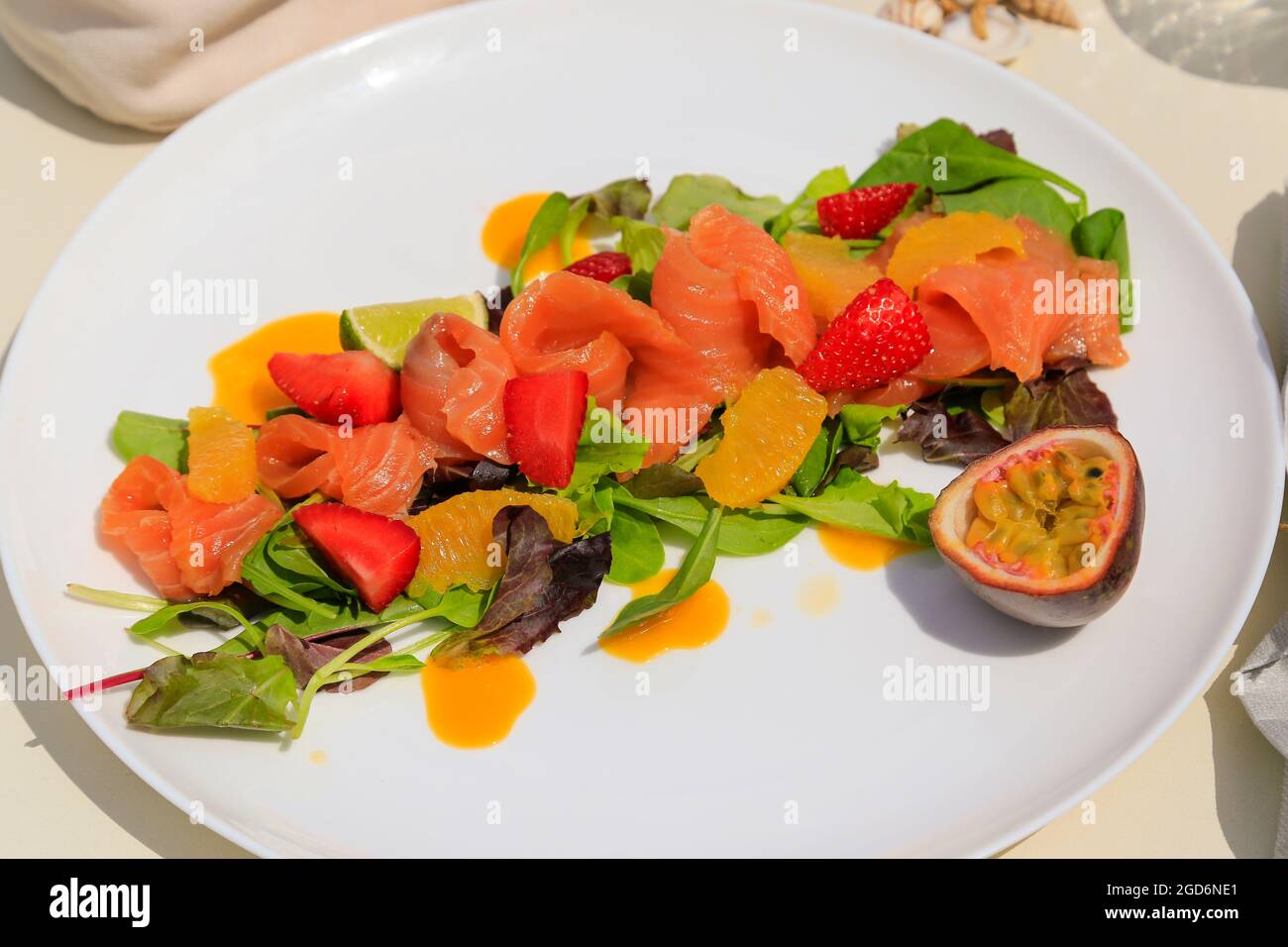 Lachs-Gravalax-Salat mit Passionsfrucht und Erdbeeren, weißer Teller. Stockfoto