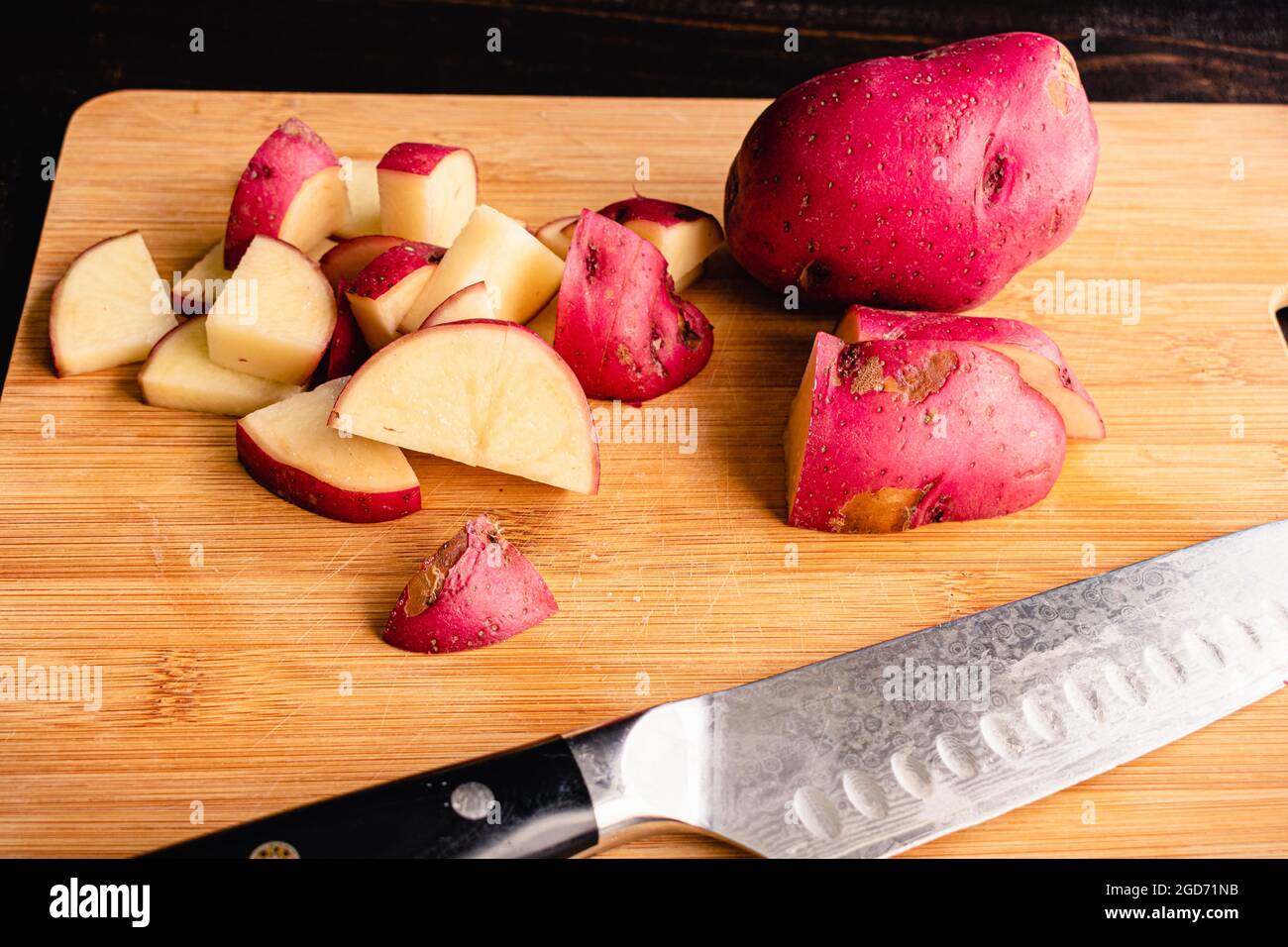 Schneiden von roten Kartoffeln in einem Bambus-Schneidebrett: Schneiden Sie rote Kartoffeln auf einem Holzschneidebrett in mundgerechte Stücke Stockfoto