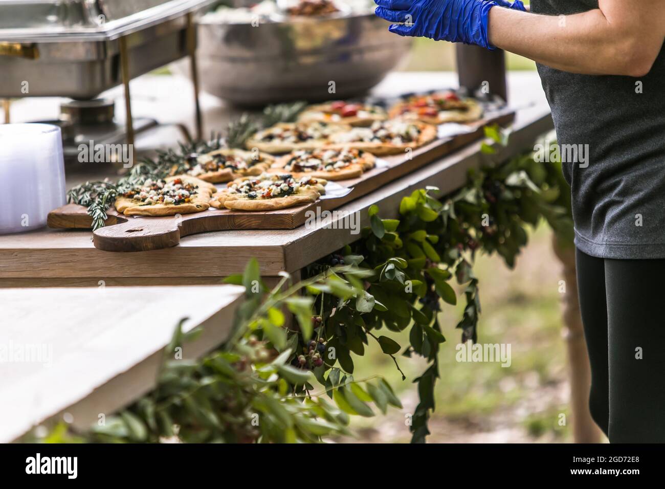 Handgemachte persönliche Pizzas auf einem Holzschneidebrett, das von einem Caterer bei einer Sommerparty im Freien hergestellt wurde Stockfoto