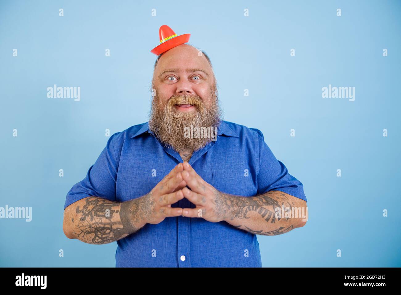 Positiver Mann mit Übergewicht trägt einen kleinen Sombrero und blaues Hemd steht auf hellblauem Hintergrund Stockfoto