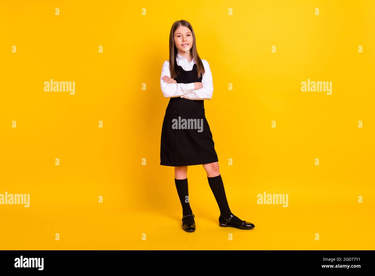 In voller Länge Foto von kleinen netten Mädchen gekreuzte Arme tragen schwarze Uniform isoliert auf gelbem Hintergrund. Stockfoto