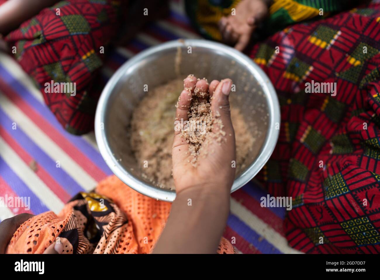 In diesem Bild nimmt die Hand eines hungrigen schwarzen afrikanischen Mädchens eine Portion Getreide aus einer Metallplatte, die mit anderen Familienmitgliedern geteilt wird; Nahrungsmangel Stockfoto