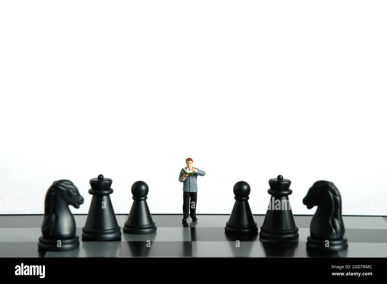 Miniatur Menschen Spielzeug Figur Fotografie. Ein männlicher Student, der über dem Schachbrett mit Bauer und Ritter steht, isoliert auf weißem Hintergrund. Bildfoto Stockfoto