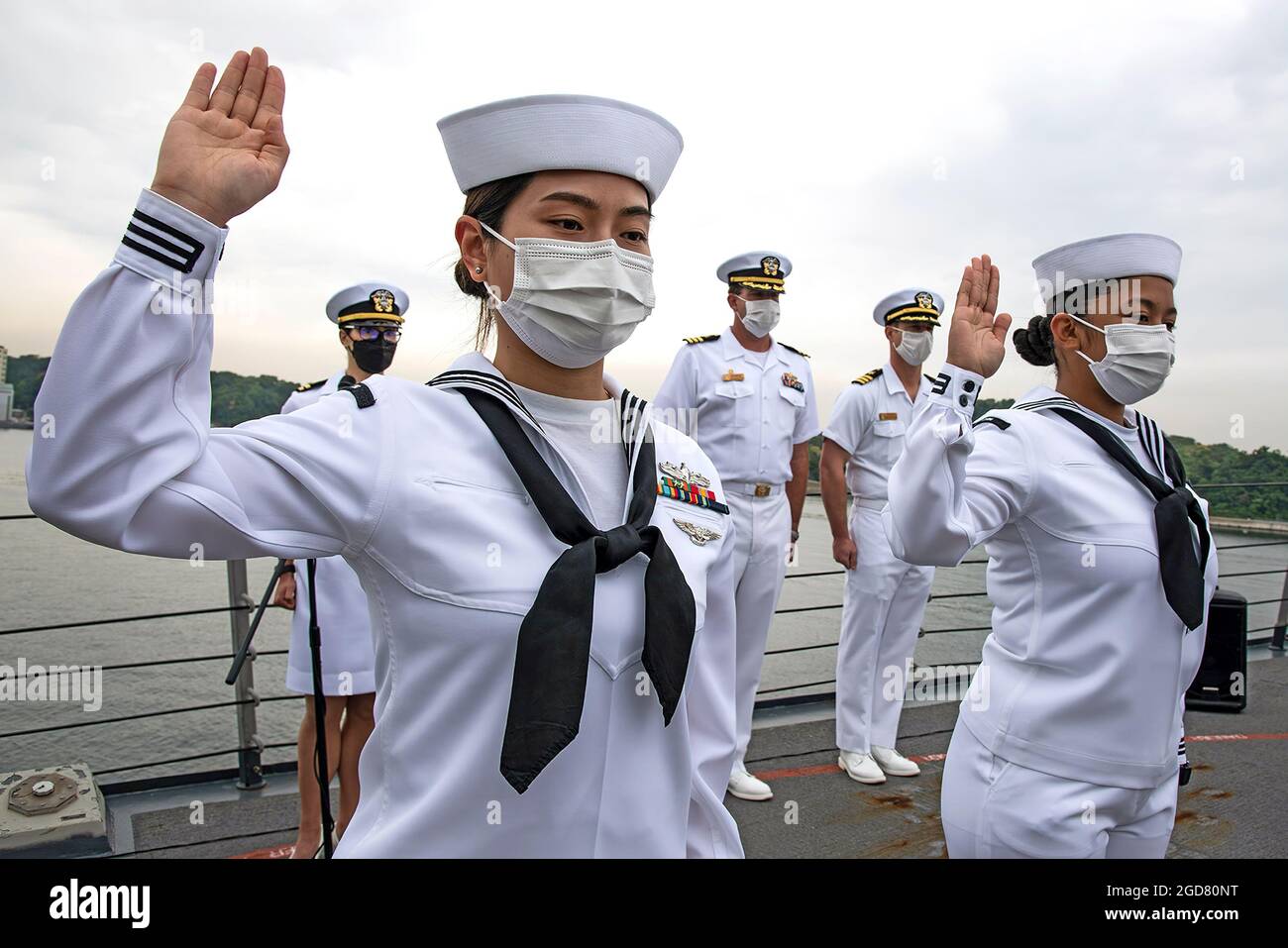 YOKOSUKA, Japan (7. Mai 2021) – Retail Specialist 3rd Class Fangfang Wen, ursprünglich aus China, links, und Retail Specialist 3rd Class Chloe Nichole Luz Rodriguez, ursprünglich aus den Philippinen, rechts, rezitieren den Schwur der Allegiance an Bord der USS Mustin (DDG 89) während einer Einbürgerung der Vereinigten Staaten von Amerika und Immigration Services (USCIS). Die Veranstaltung war die erste Einbürgerungszeremonie an Bord eines aktiven US-Navy-Schiffes während der COVID-19-Pandemie. Mustin wird nach Japan entsandt und bei Commander Fleet Activities Yokosuka (CFAY) als Teil der 7. US-Flotte stationiert. Für Stockfoto