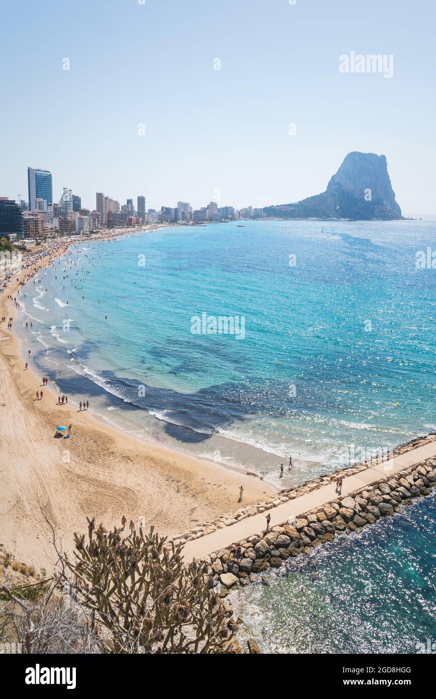 Touristen, die am Strand und Pier entlang der Küste von Calpe mit Blick auf die Felsformation 'ifach', Costa Blanca, Spanien, spazieren Stockfoto