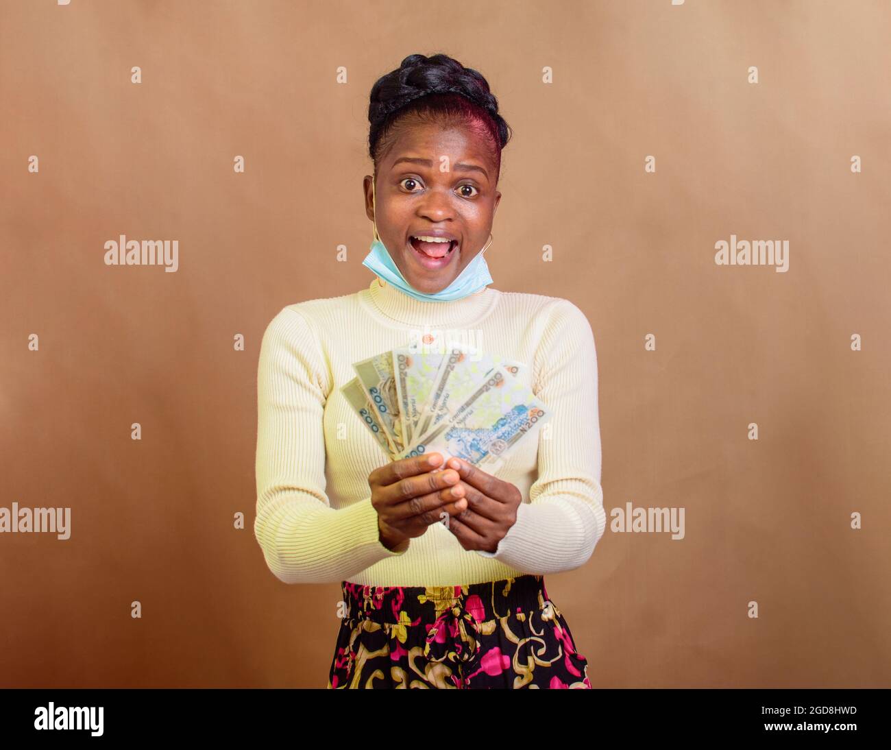 Fröhliche, süße afrikanische Dame mit Nasenmaske, die mehrere Naira-Scheine, Bargeld, nigerianische Währung oder Geld für Transaktionen in ihren Händen hält Stockfoto