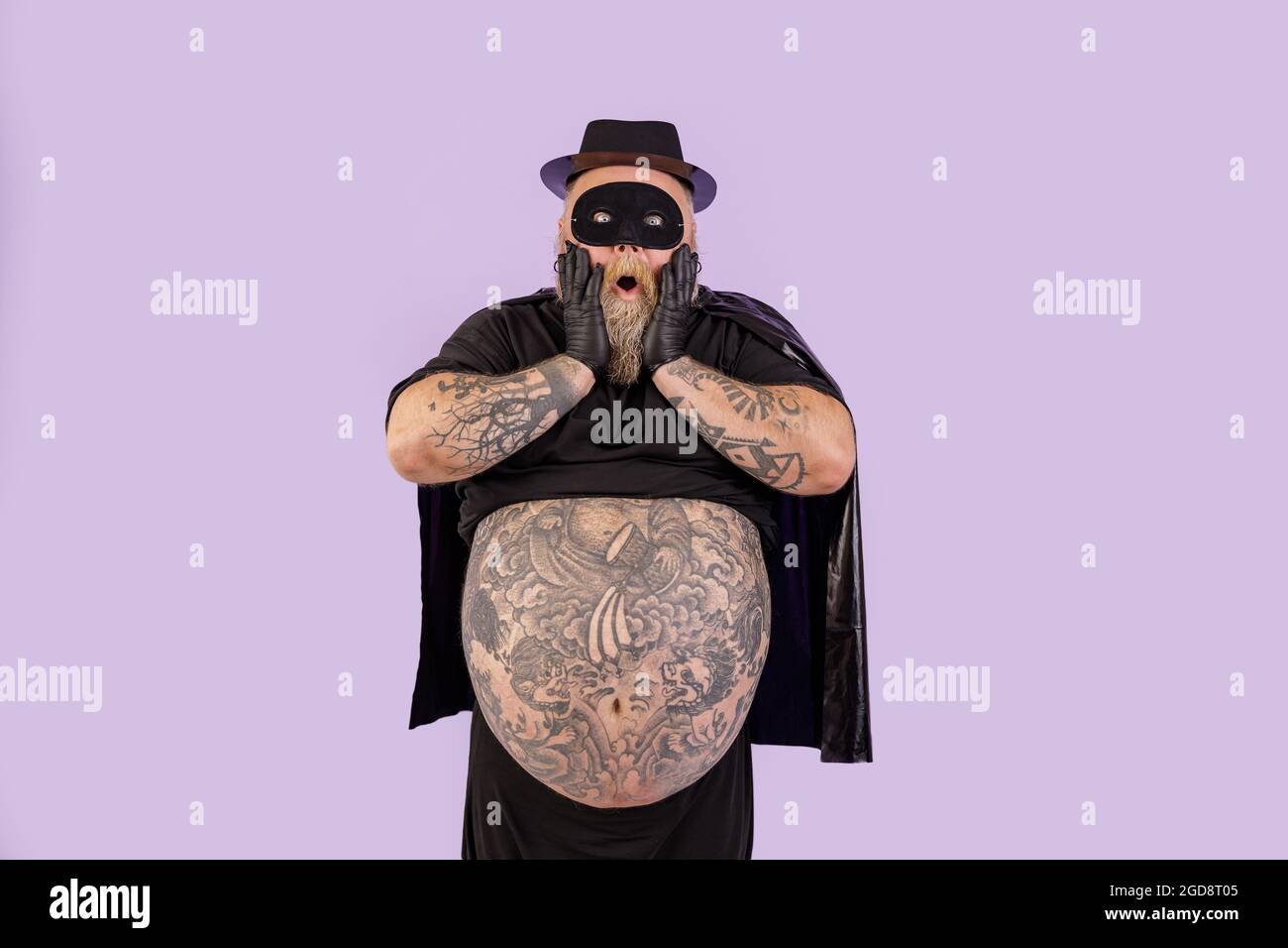 Schockiert plump Mann im Helden Kostüm hält Wangen stehen auf lila  Hintergrund Stockfotografie - Alamy