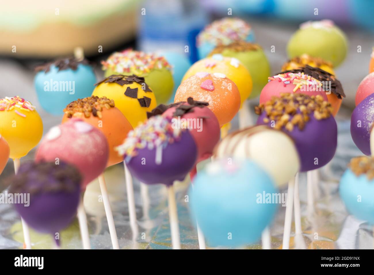 Eine lebendige Auswahl an bunten Kuchen-Pops, dekoriert mit Streuseln und Schokoladenstückchen, auf einem festlichen Tisch. Stockfoto