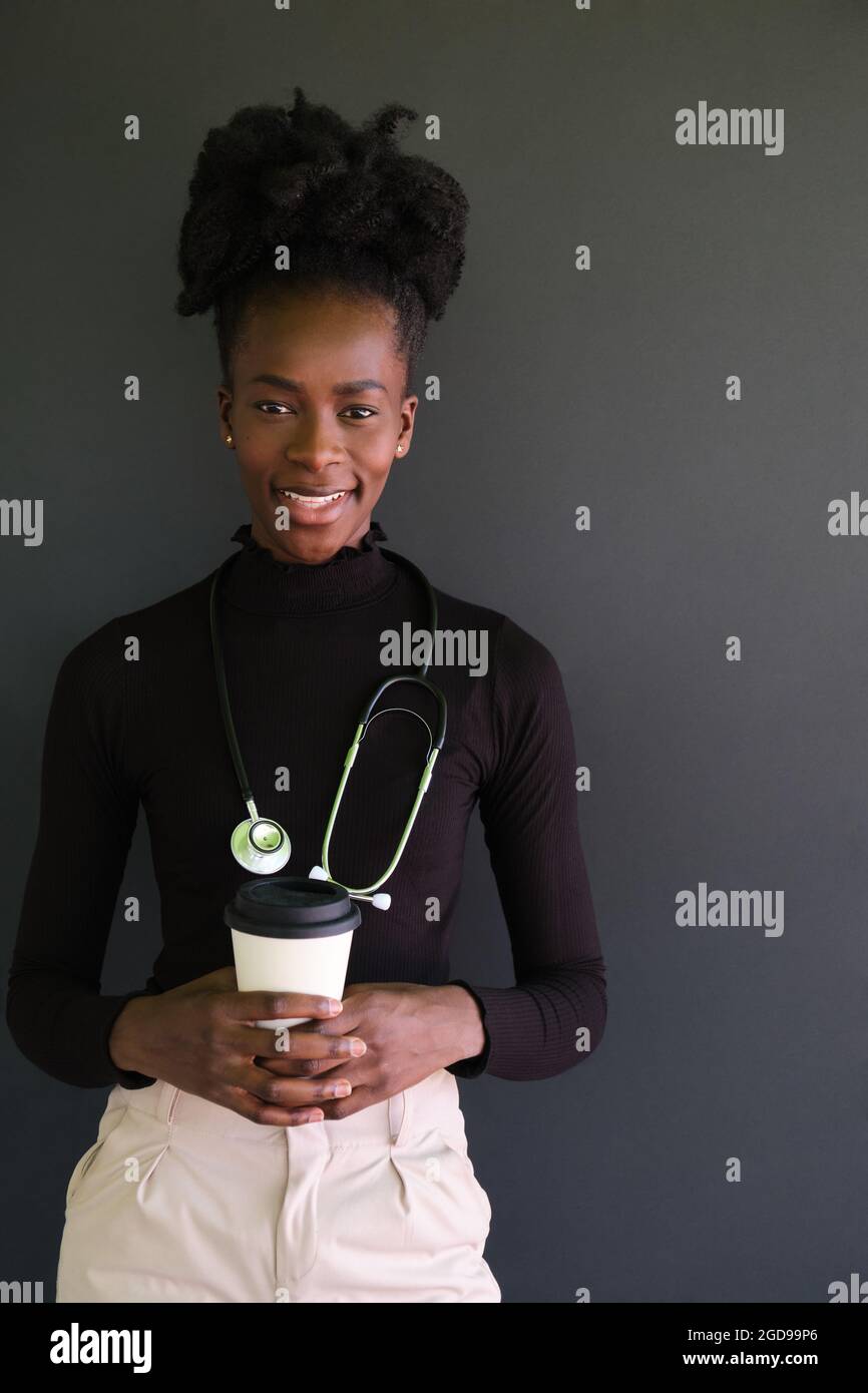 Lächelnde afrikanische Ärztin mit Stethoskop und einer Tasse Kaffee. Stockfoto