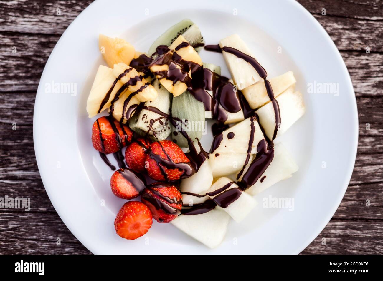 Köstlicher Obstsalat mit Schokoladenüberzug auf Holzbank Stockfoto