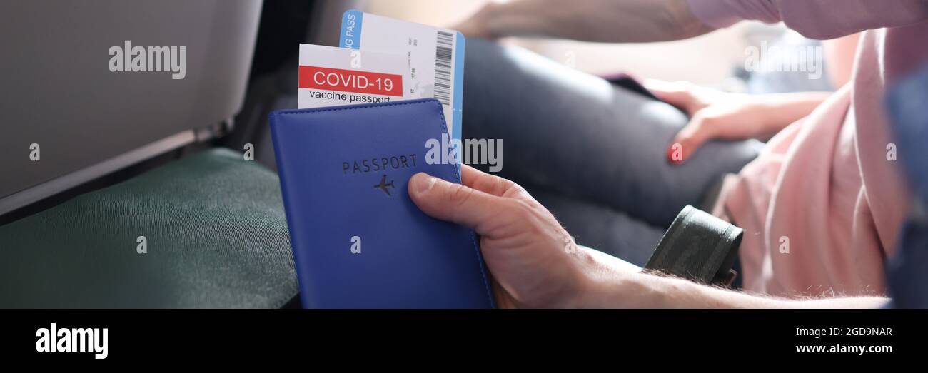 Mann, der im Flugzeug fliegt und einen Impfpass gegen Covid 19 hält und Tickets aus der Nähe hält Stockfoto